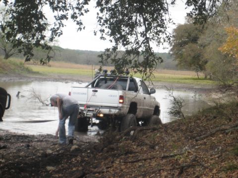 2001 Jeep Wrangler - A white pickup truck is stuck in the mud and water, with a person attempting to assist.