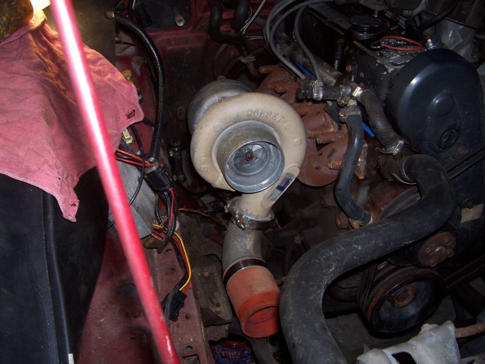 Engine bay with a turbocharger, hoses, and wiring. A red cloth is draped over parts