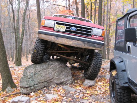 1990 Ford Bronco - A red Ford truck navigates a rocky trail, with another vehicle visible to the right.