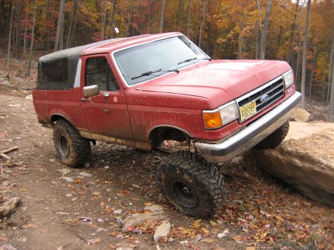 1990 Ford Bronco - This red Ford Bronco is navigating a rocky off-road trail during autumn.