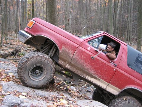1990 Ford Bronco - Red Ford Bronco navigating a rocky, wooded off-road course.