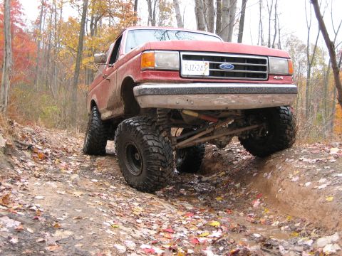 1990 Ford Bronco - 1990 Ford Bronco navigating a muddy trail with fallen autumn leaves.