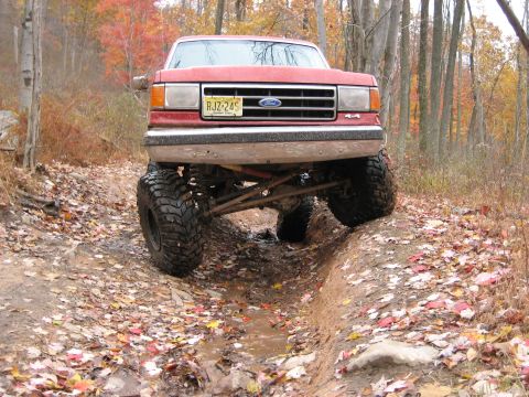 1990 Ford Bronco - A lifted red Ford truck navigates a challenging off-road trail during autumn.