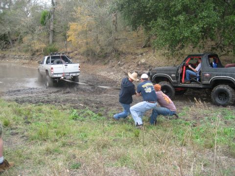 2001 Jeep Wrangler - Two vehicles are engaged in an off-road recovery operation, with one truck stuck in the mud and the other pulling it out.