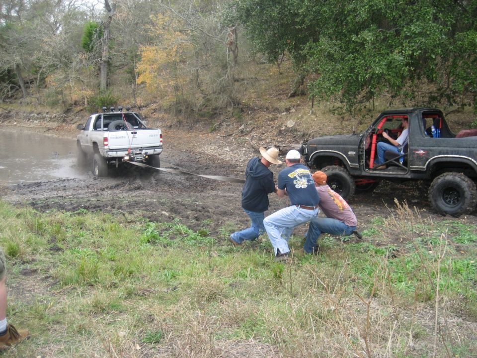 White pickup truck stuck in mud, being towed by black SUV