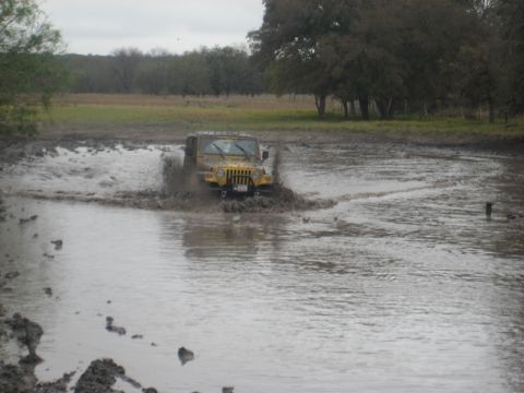 2001 Jeep Wrangler - A yellow 2001 Jeep Wrangler navigates through a muddy off-road course, kicking up water.