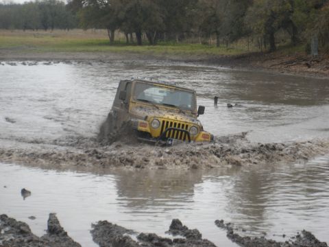 2001 Jeep Wrangler - A yellow 2001 Jeep Wrangler navigates a muddy off-road course, splashing water as it goes.