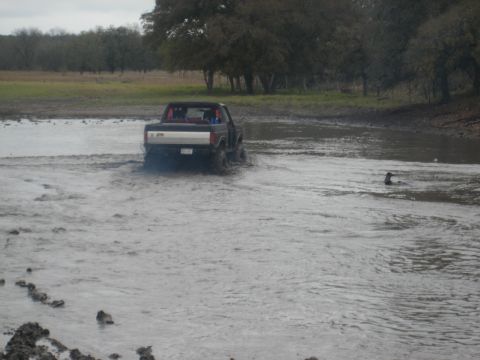 2001 Jeep Wrangler - A truck navigates through a muddy, watery terrain with trees in the background.