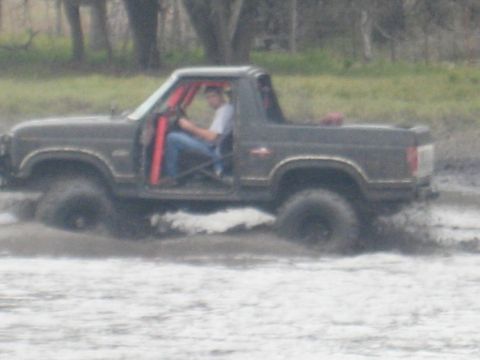2001 Jeep Wrangler - This dark brown SUV, equipped with a red roll cage, navigates through a muddy terrain, kicking up water and mud as it goes.