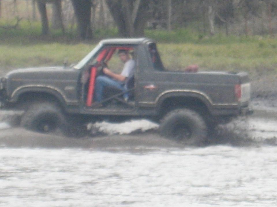 Dark brown off-road SUV with red roll cage driving through mud