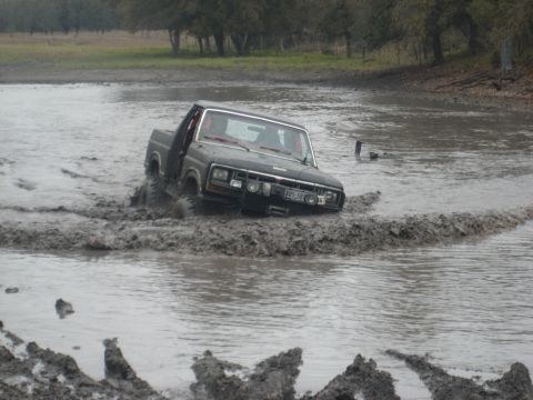 2001 Jeep Wrangler - This truck is navigating a challenging muddy terrain, with water splashing around its tires.