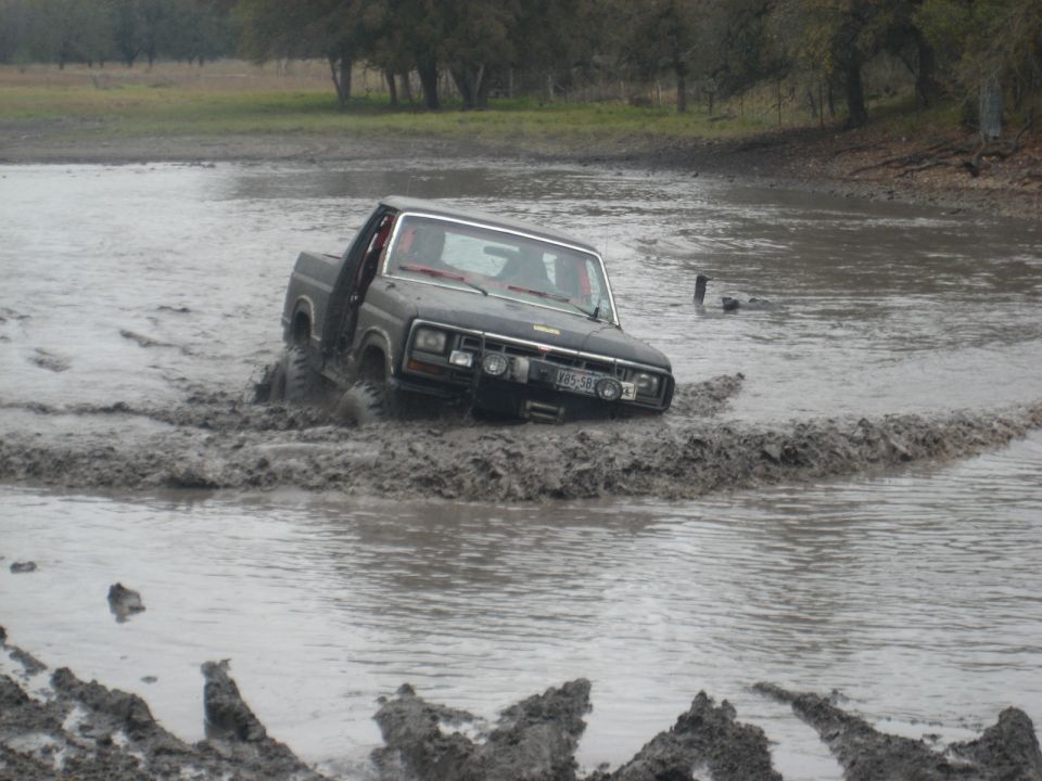 Black pickup truck driving through a muddy water hole, tires deep in the muck