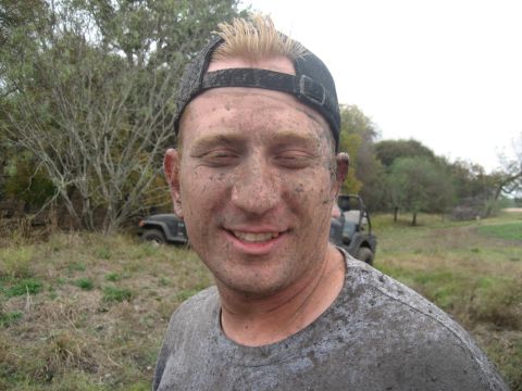 2001 Jeep Wrangler - A man, covered head to toe in mud, smiles with his eyes closed while a muddy Jeep Wrangler sits in the background.