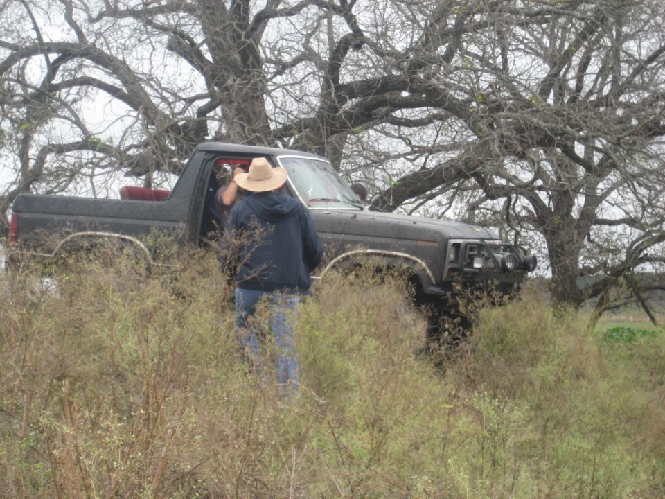 Black Ford Bronco II parked in brush with two people near the driver's side door