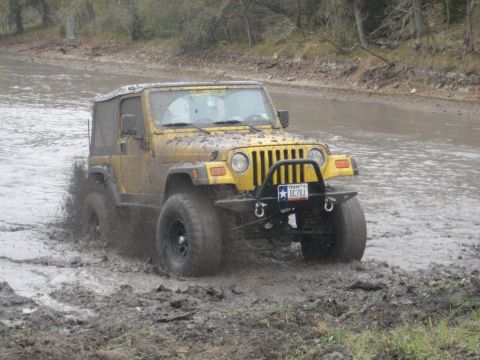 2001 Jeep Wrangler - A yellow 2001 Jeep Wrangler navigates a muddy off-road course, kicking up water and mud.