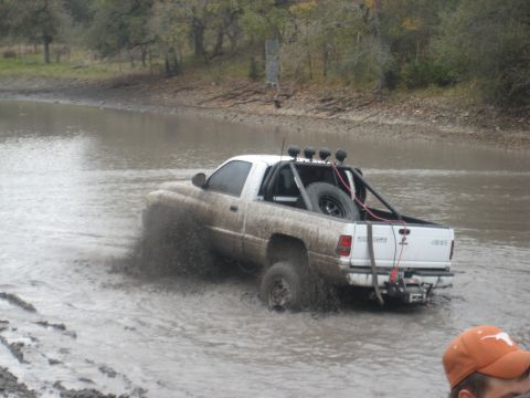 2001 Jeep Wrangler - White pickup truck navigates through a muddy body of water, kicking up spray.