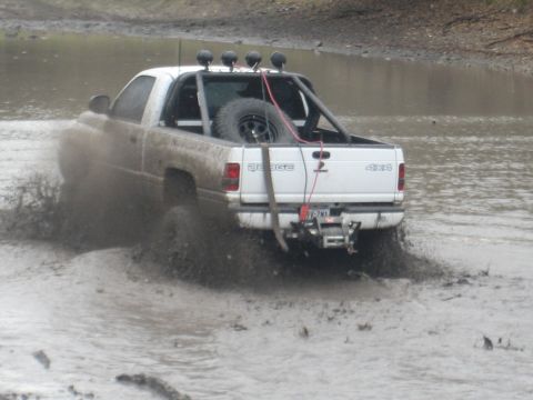 2001 Jeep Wrangler - A white Dodge pickup truck navigates through a muddy terrain, kicking up a significant amount of mud and water.
