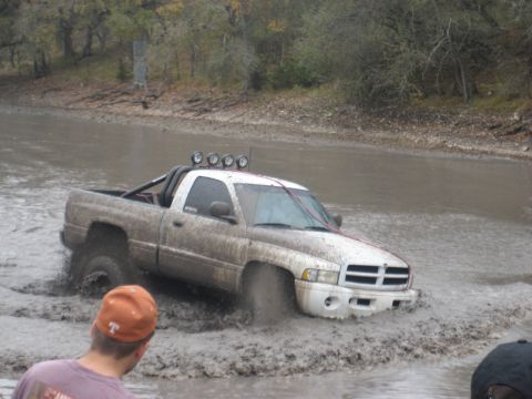 2001 Jeep Wrangler - A white Dodge Ram pickup truck is stuck in thick mud, with its front end submerged.