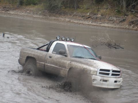 2001 Jeep Wrangler - White Dodge Ram pickup truck navigates through a muddy terrain, kicking up water and mud.