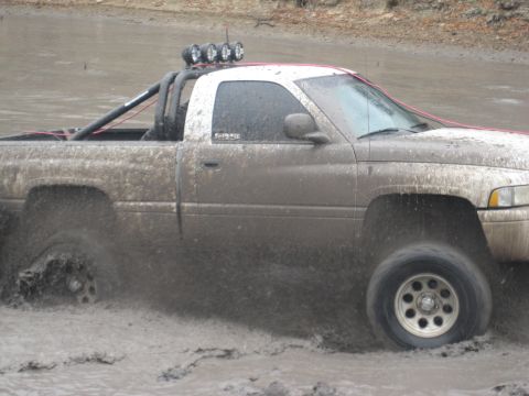 2001 Jeep Wrangler - Pickup truck navigates through a muddy water obstacle, kicking up spray.