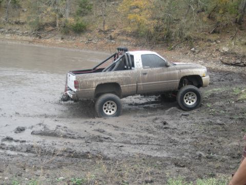 2001 Jeep Wrangler - A lifted pickup truck navigates a muddy terrain, kicking up dirt and water.