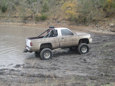2001 Jeep Wrangler - A lifted pickup truck navigates a muddy terrain near a body of water.
