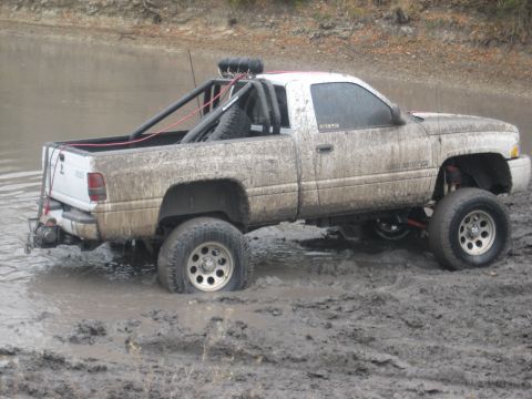 2001 Jeep Wrangler - A white pickup truck is stuck in deep mud, with a roll cage and spare tire visible in the bed.