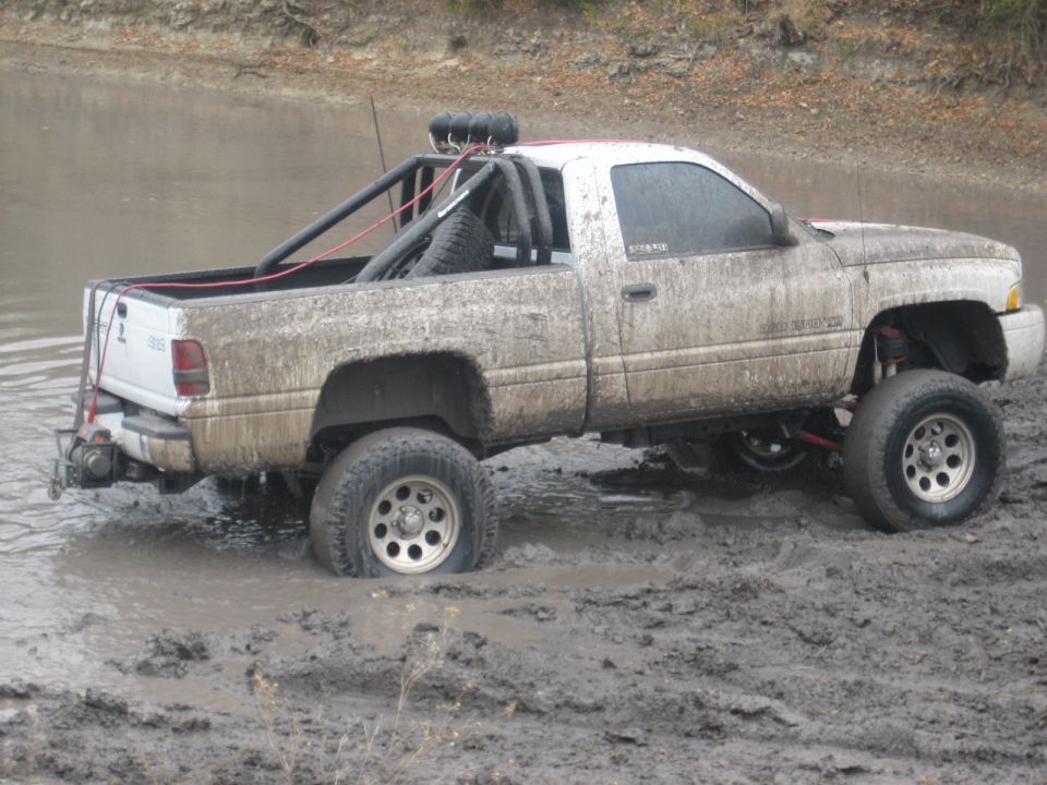 White pickup truck stuck in mud, rear-mounted spare tire, roll cage