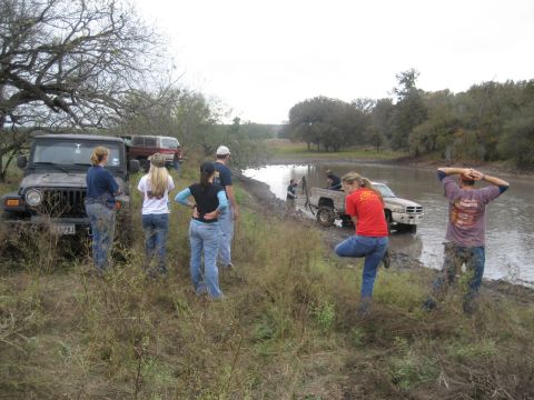 2001 Jeep Wrangler - Several people stand around a muddy Jeep Wrangler and a Dodge Ram pickup truck stuck in a muddy area.