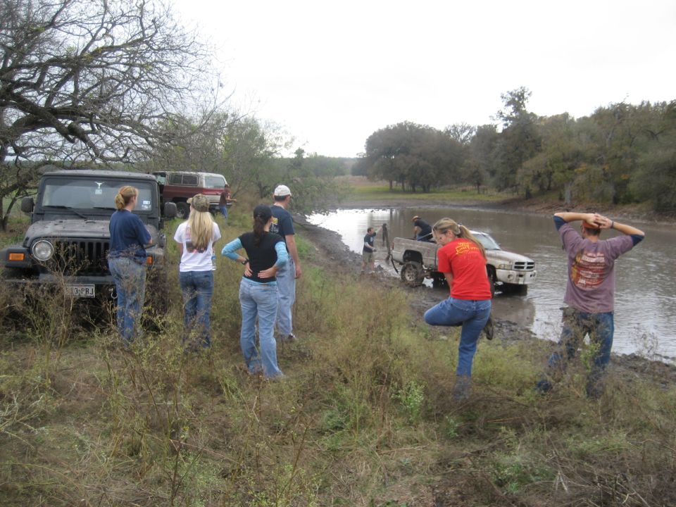 Muddy 2001 Jeep Wrangler parked on grassy bank next to a muddy ditch with people standing around