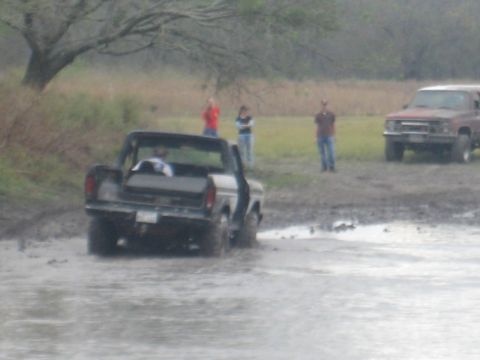 2001 Jeep Wrangler - Two trucks are stuck in the mud with people standing around.