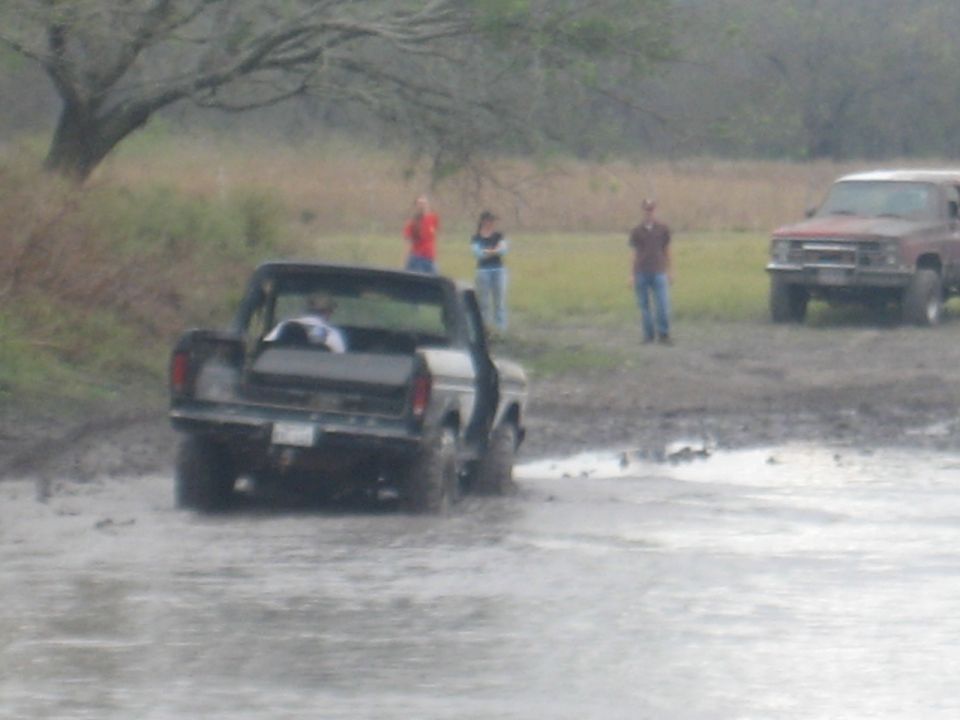 Black pickup truck stuck in mud with a red truck in the background