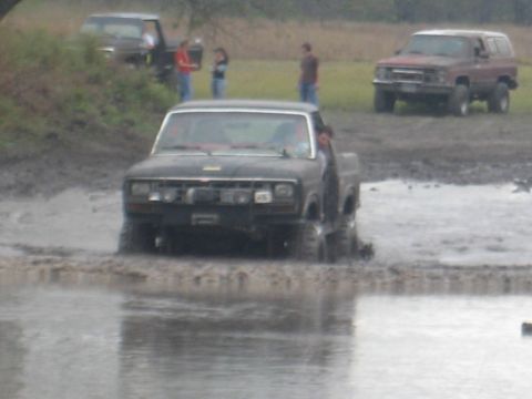 2001 Jeep Wrangler - A black pickup truck navigates a muddy terrain, with other vehicles and people visible in the background.