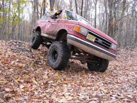 1990 Ford Bronco - Red 1990 Ford Bronco navigating an off-road trail covered in autumn leaves.