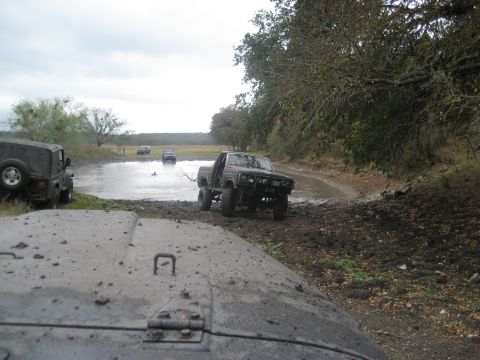2001 Jeep Wrangler - Several off-road vehicles navigate a muddy, water-filled trail under an overcast sky.