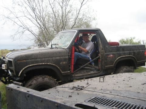 2001 Jeep Wrangler - A muddy black Ford Bronco II with a roll cage is seen off-road with another vehicle in the foreground.