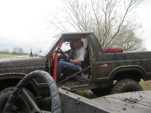 2001 Jeep Wrangler - Two individuals are inside a modified black truck, which appears to be an off-road vehicle, with another vehicle partially visible in the f…