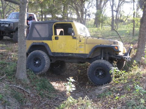 2001 Jeep Wrangler - A yellow 2001 Jeep Wrangler is seen off-roading with another vehicle in the background.