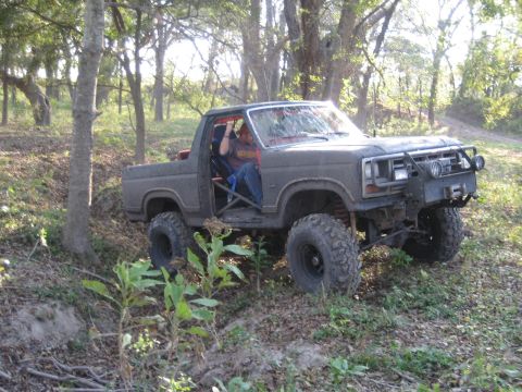 2001 Jeep Wrangler - An off-road truck with a roll cage is parked on a dirt path surrounded by trees.