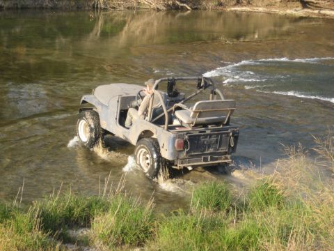 2001 Jeep Wrangler - A blue Jeep CJ-7 navigates a shallow river, kicking up water as it moves forward.