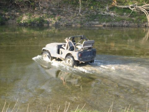 2001 Jeep Wrangler - A gray Jeep CJ-7 navigates a shallow river, kicking up water as it goes.