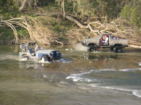2001 Jeep Wrangler - Two off-road vehicles navigate a rocky riverbed surrounded by trees.