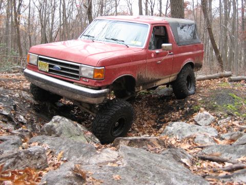 1990 Ford Bronco - This red 1990 Ford Bronco is navigating a rocky, wooded terrain.