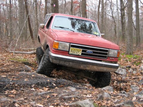 1990 Ford Bronco - This red Ford Bronco is shown off-roading on a rocky trail in a wooded area.