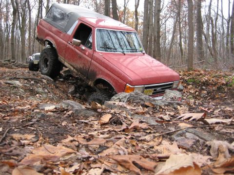 1990 Ford Bronco - 1990 Ford Bronco tackling an off-road trail with another vehicle visible behind it.