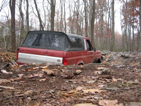 1990 Ford Bronco - A red Ford Bronco is stuck in the mud and leaves on a wooded trail.