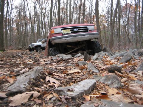 1990 Ford Bronco - This red SUV is navigating a difficult rocky trail with a white Jeep following behind.