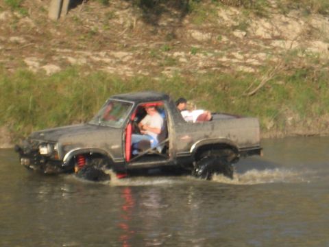 2001 Jeep Wrangler - Off-road pickup truck navigates through a muddy waterway with occupants.