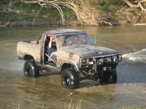 2001 Jeep Wrangler - A heavily modified pickup truck navigates a shallow river with its doors open.