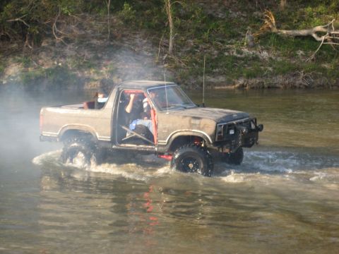 2001 Jeep Wrangler - This lifted off-road truck navigates through a shallow body of water, creating a spray as it moves.